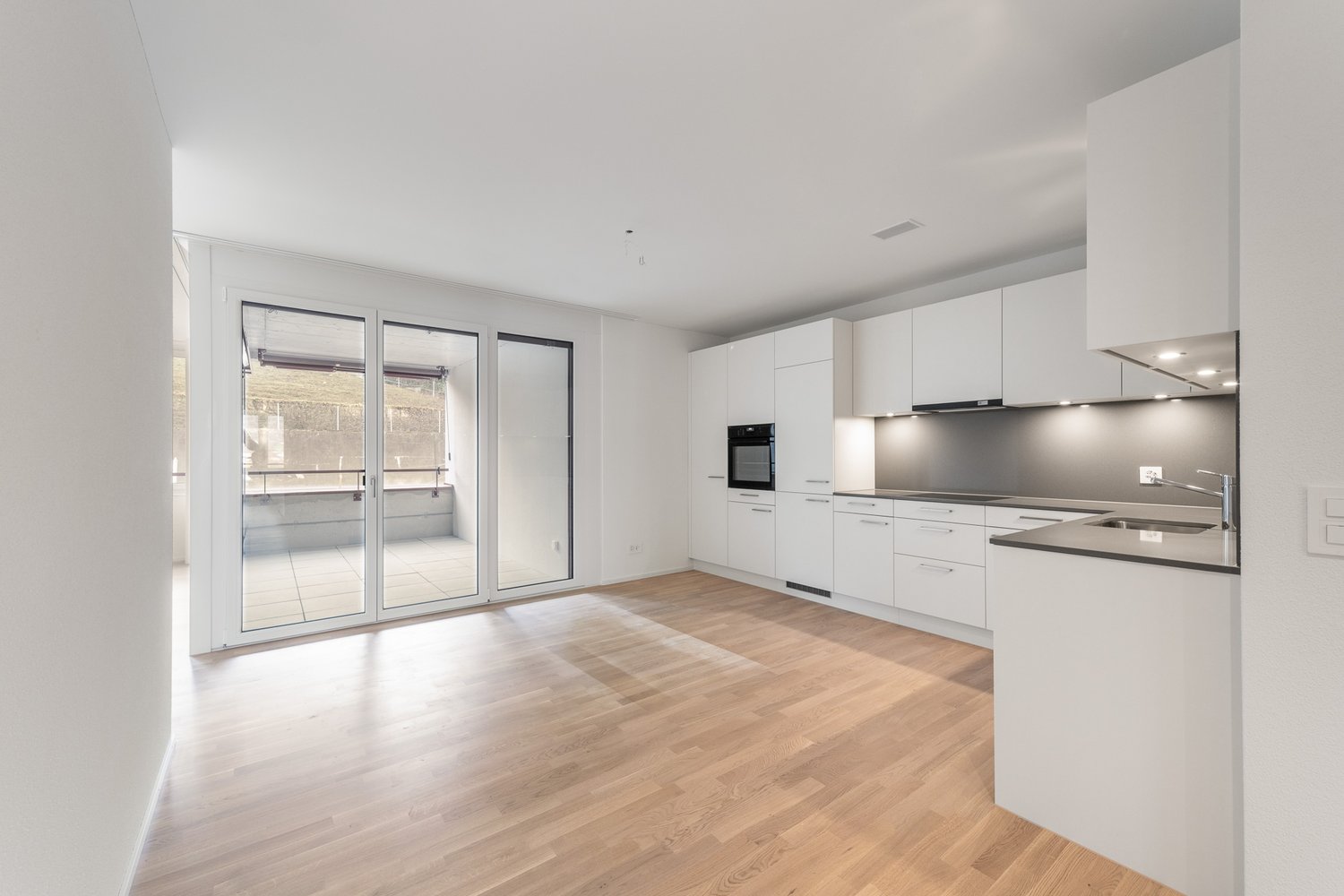 kitchen with white cabinets, black countertops, sliding glass door, balcony, wooden floors