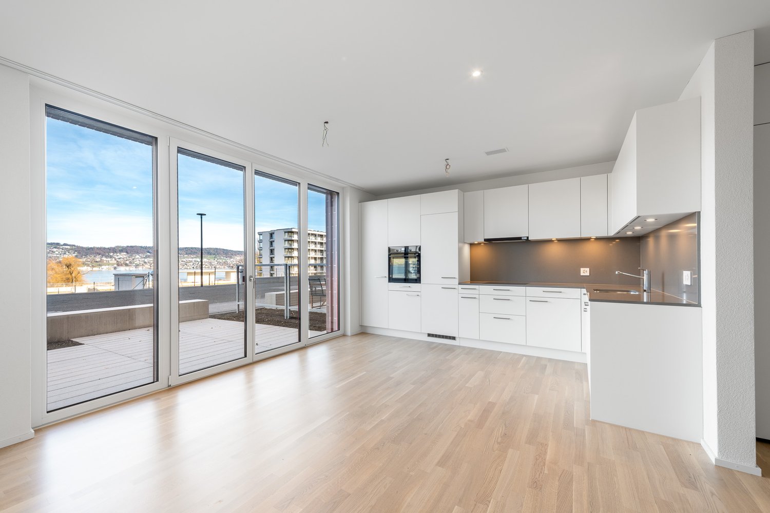 modern apartment with large windows, glass sliding doors leading to balcony, white kitchen cabinets, wooden floor, open concept living space