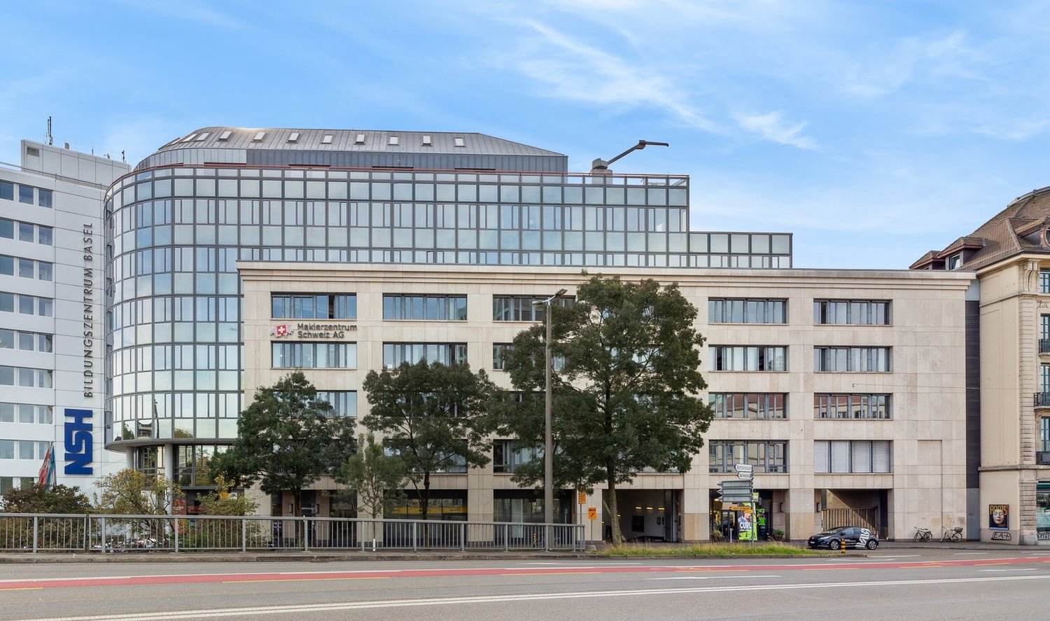Modern office building with glass facade, multiple floors, entrance with glass doors, street with cars and bicycles