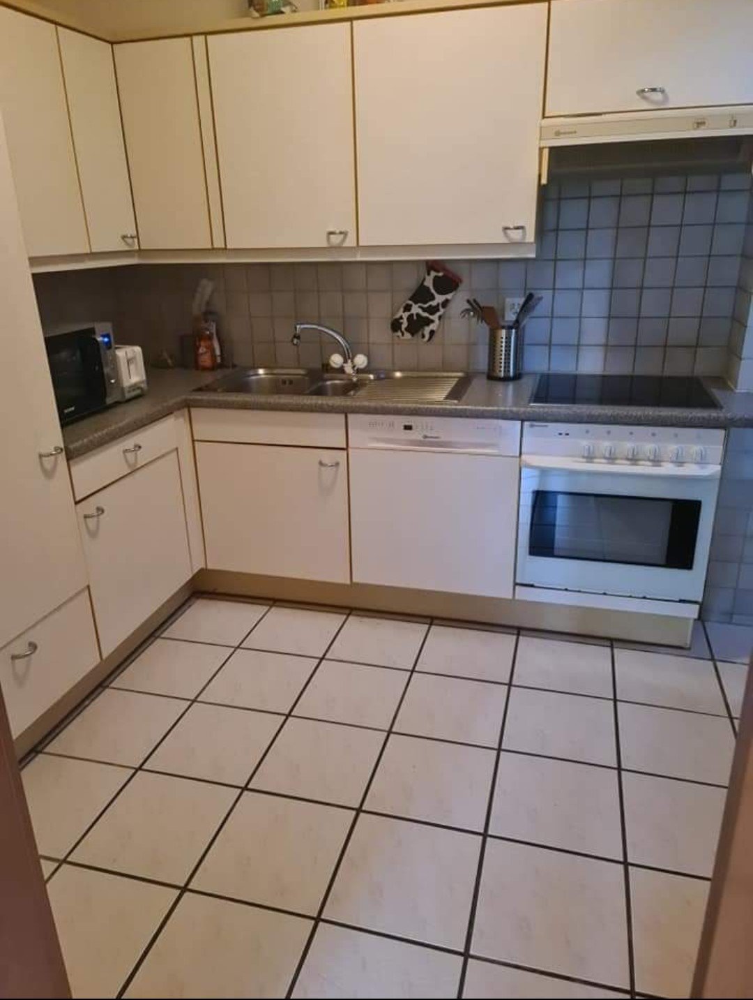 white tiled floor, white cabinets, black tiled wall, white sink, dishwasher, microwave, oven, countertop, silver appliances