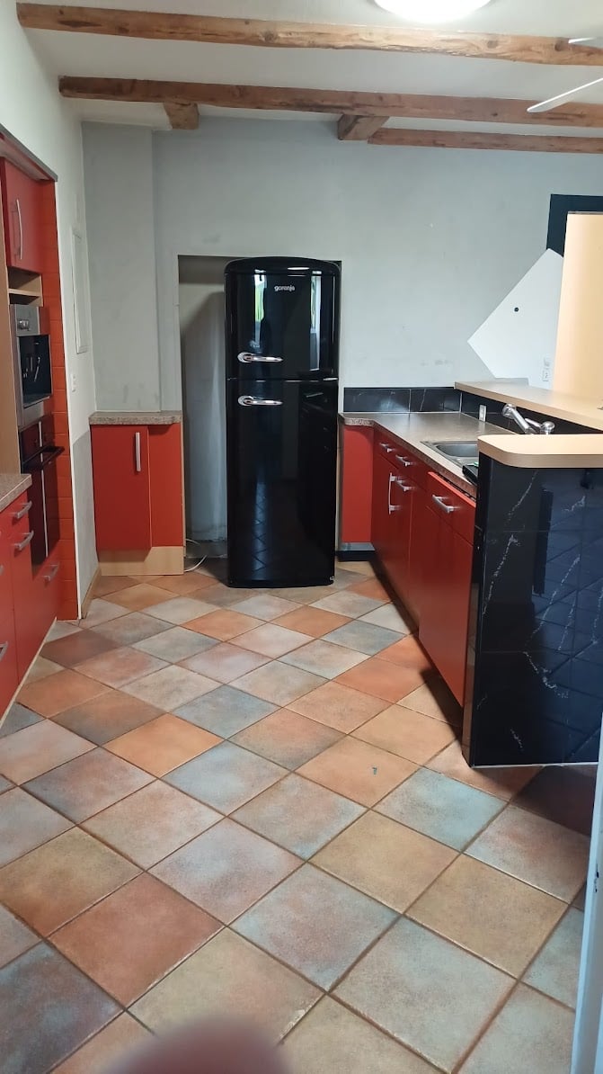 Modern kitchen with tiled floor, black refrigerator, red cabinets, white walls, a sink with faucet, a gas stove, and a fan on the ceiling