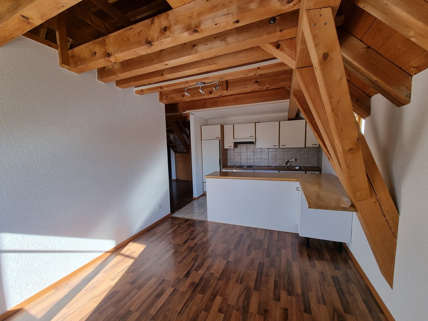 Open kitchen with wooden beams, white cabinets, wooden countertop, white walls, wooden floor