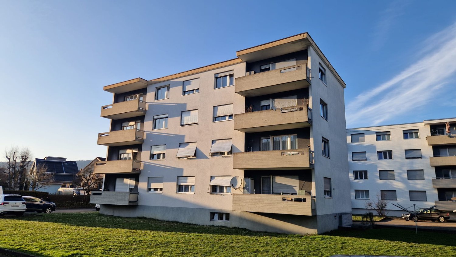 5-story apartment building, concrete balconies, flat roof, multiple windows, outdoor parking area