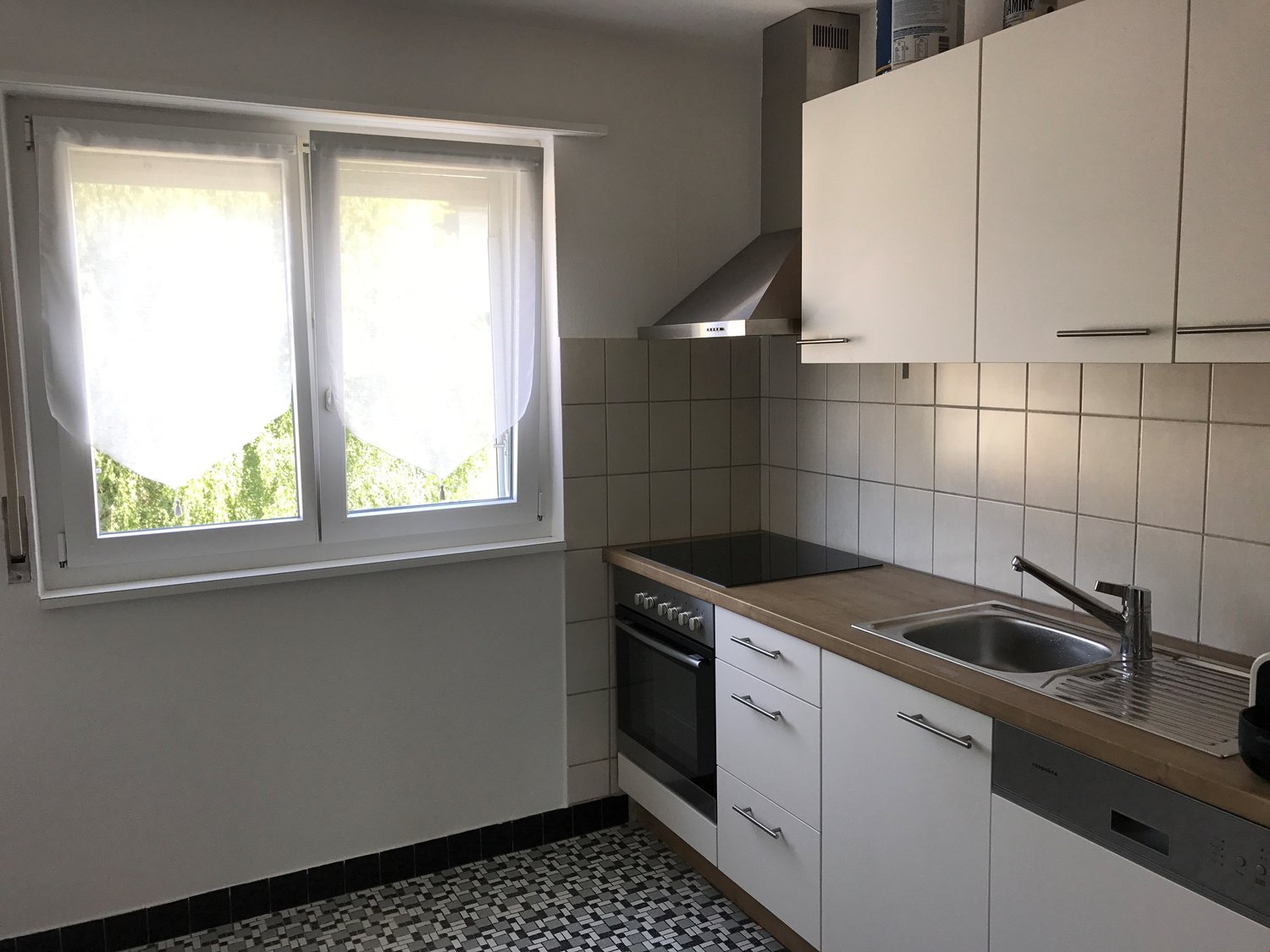 white cabinets, white countertop, stainless steel sink, oven and stove, range hood, tiled wall, window with curtain