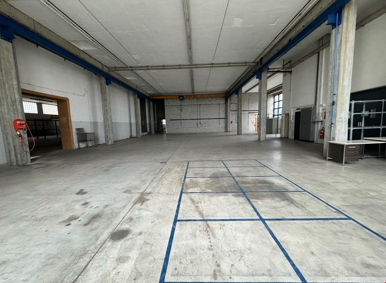 large room with high ceiling, blue lines on the floor, concrete walls, some equipment and furniture