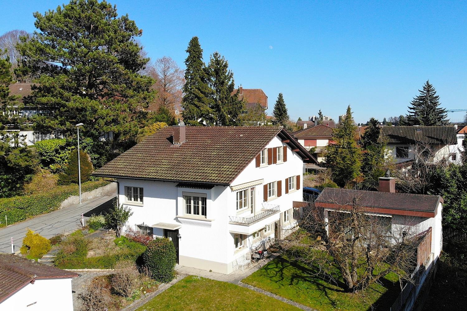 House: white exterior, brown roof, multiple windows, balconies, yard with plants, street light