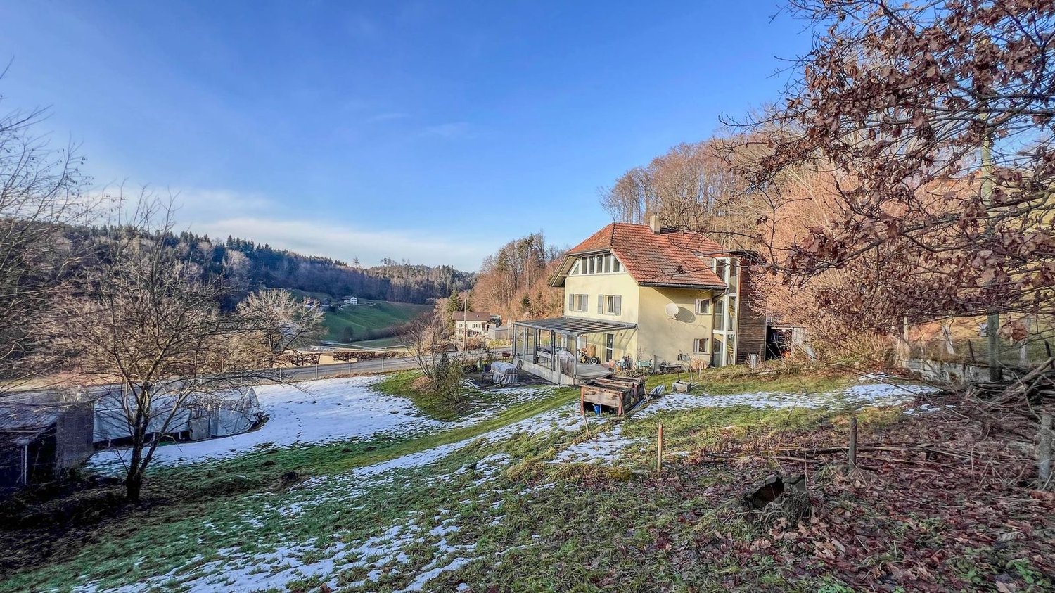 Detached house with red roof, glass windows, snow on the ground, trees, mountains, clear blue sky