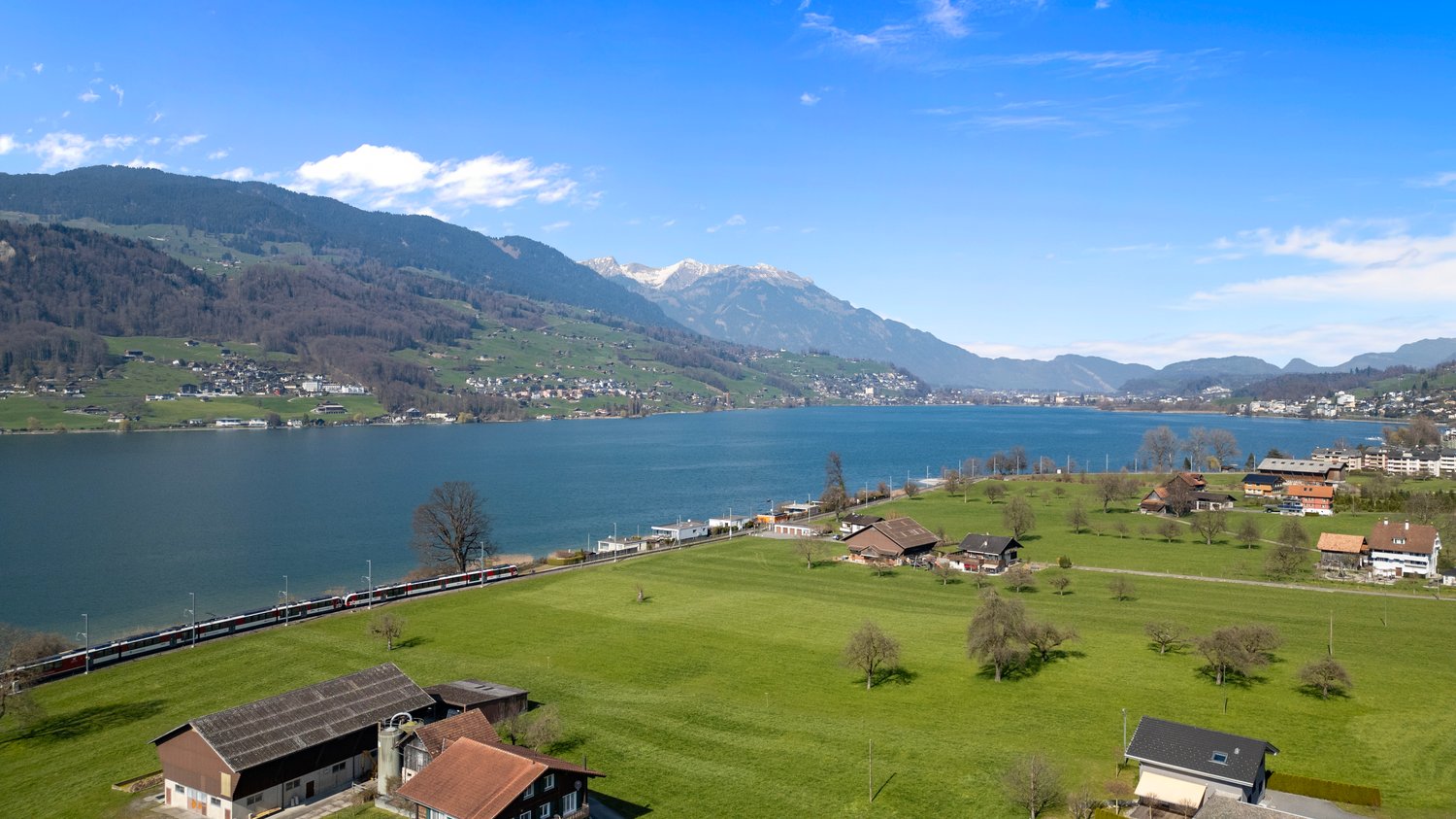 Aerial view of a lake, mountains, houses, and a train on the tracks