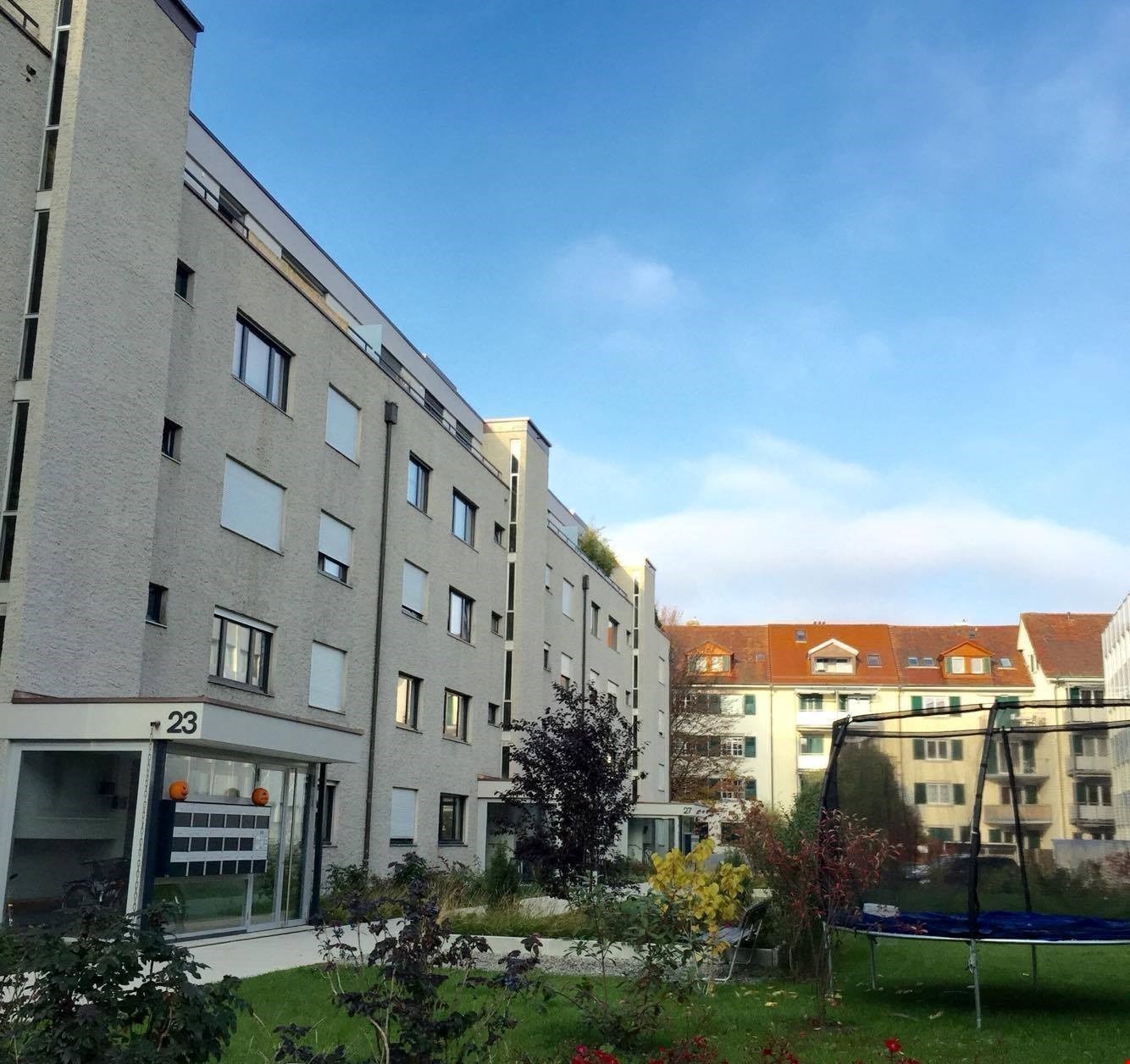 4 story building, balcony, garden with plants and grass, orange house in the background