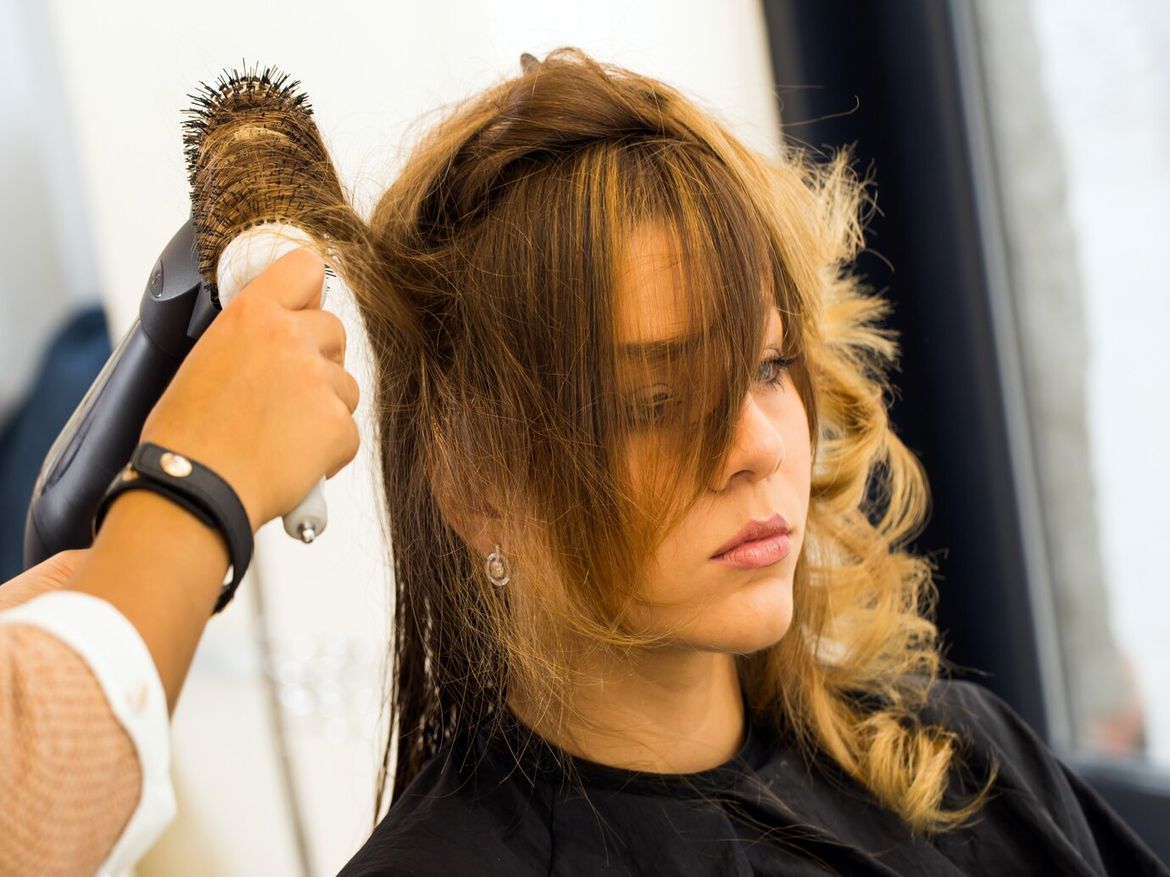 A woman with long blonde hair is getting her hair dried by a hair stylist using a hair dryer.