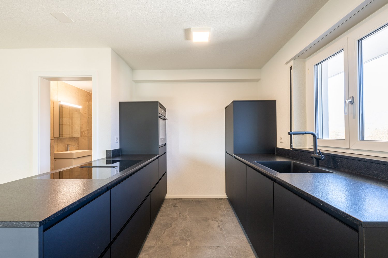 modern kitchen with black countertops, black cabinets, induction cooktop, oven, sink, faucet, window