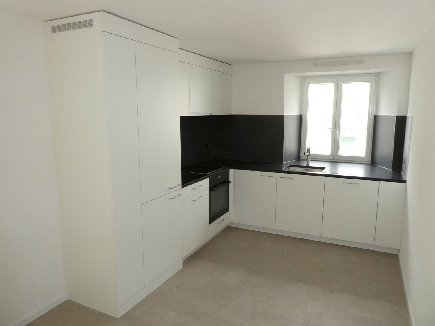 Modern, minimalist kitchen with white cabinets, black countertops, built-in oven, and dishwasher. Large windows provide natural light.
