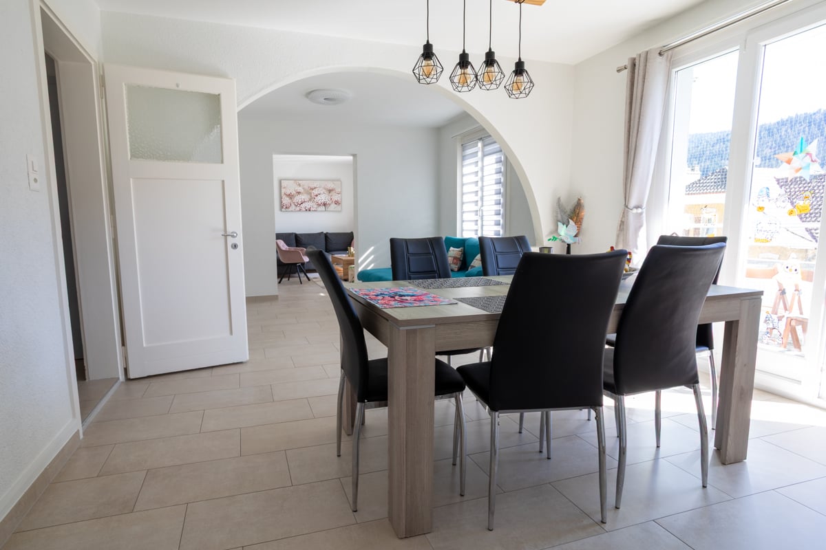 Dining room with a table and chairs, white walls, tiled floor, large windows, and a view of the outside