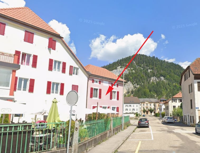 A street view of a building with red shutters and a green fence, with a mountain in the background.