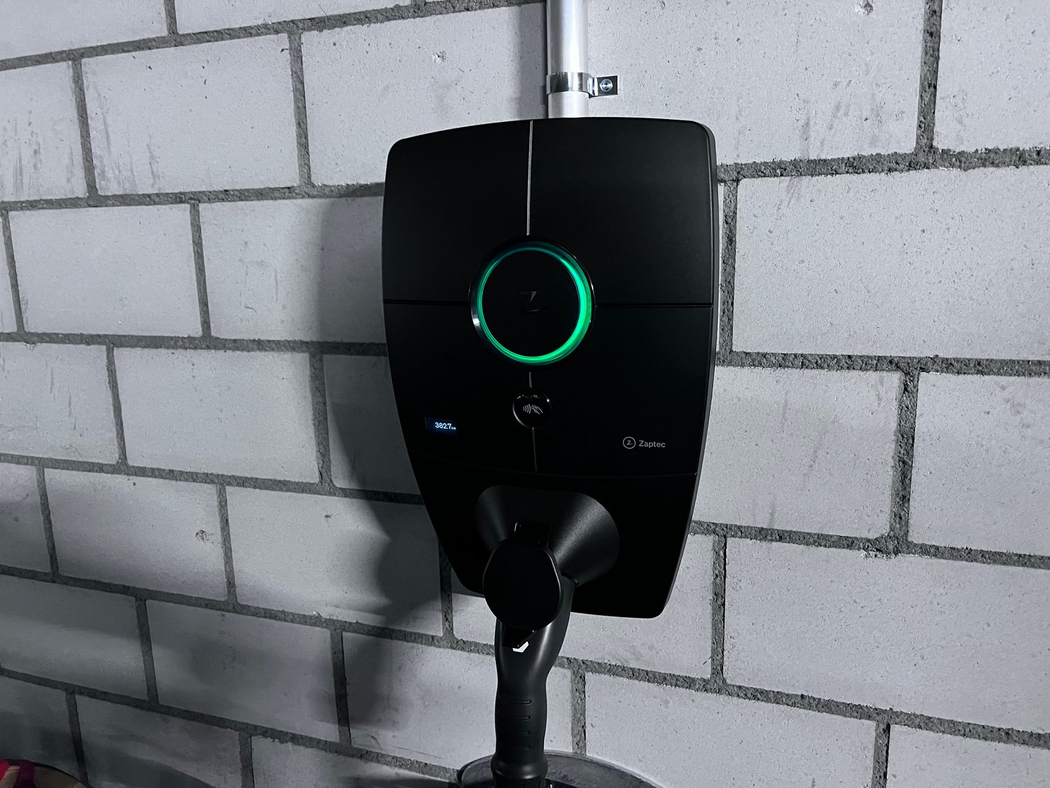 Black electric vehicle charging station with a green LED ring light, mounted on a concrete wall