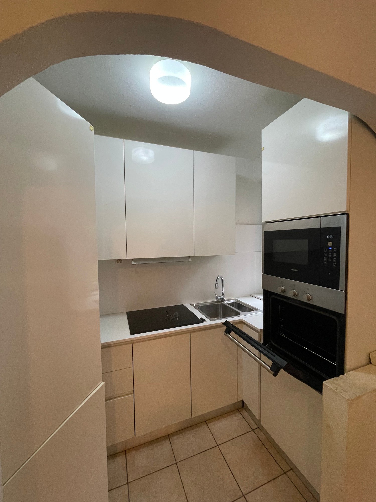 Modern kitchen with white cabinets, tile flooring, microwave, sink, gas stove, and oven