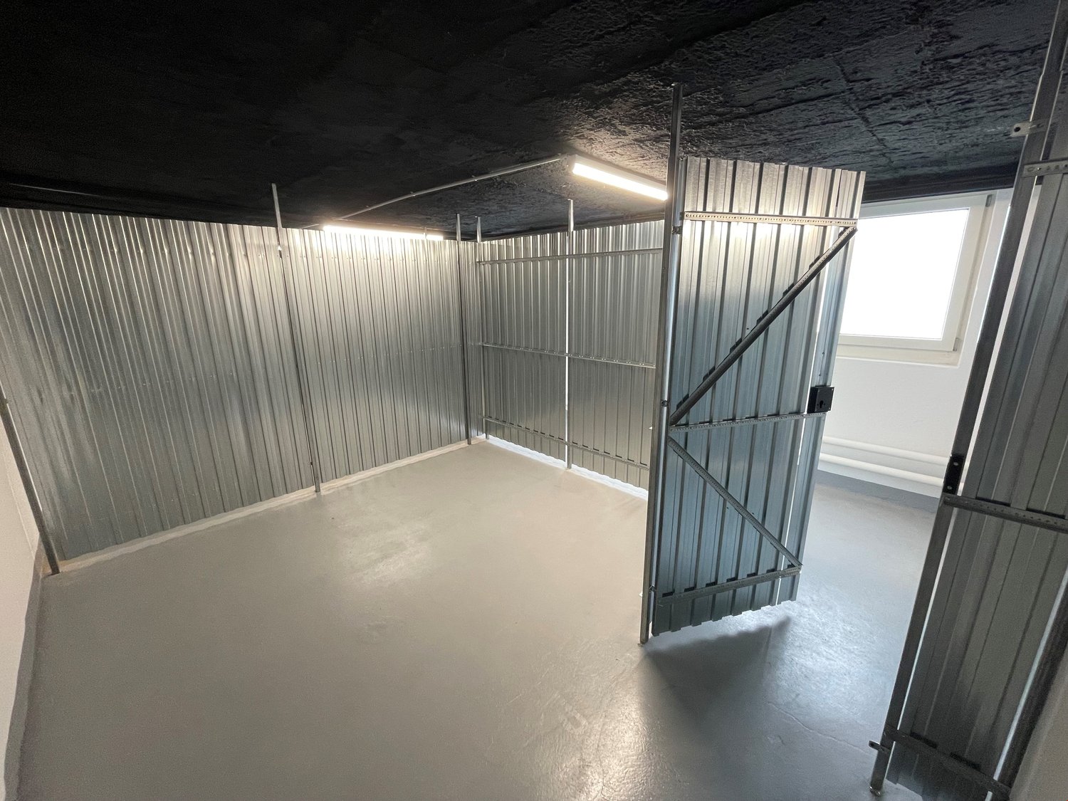 Empty room with metal walls, concrete floor, and two metal doors.