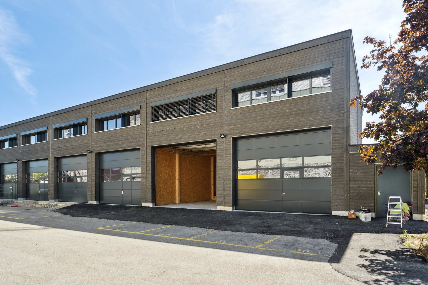 Industrial building with multiple garages, gray exterior, windows, and an open garage door.
