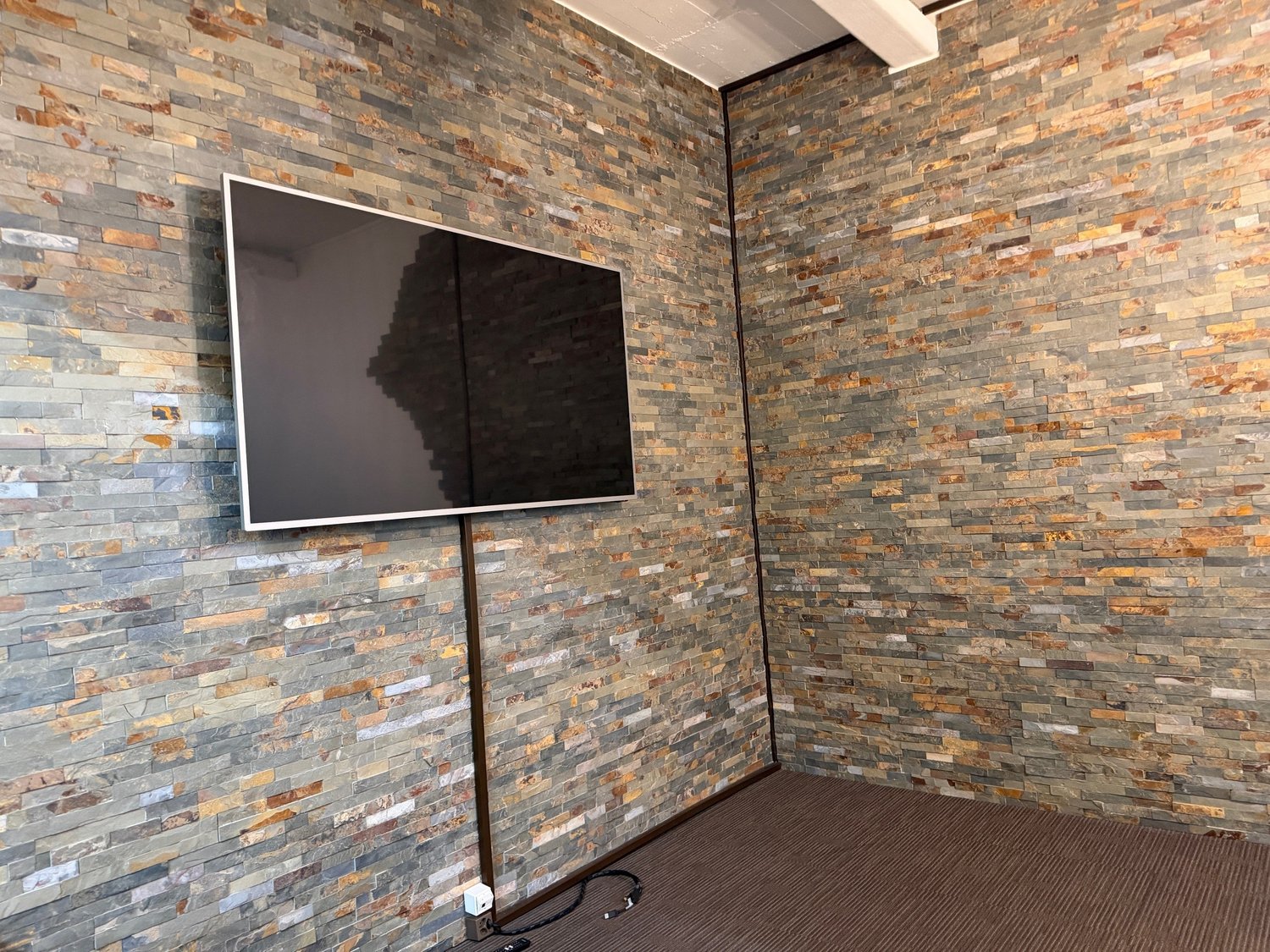 room with a large television mounted on the wall, stone brick walls, carpeted floor
