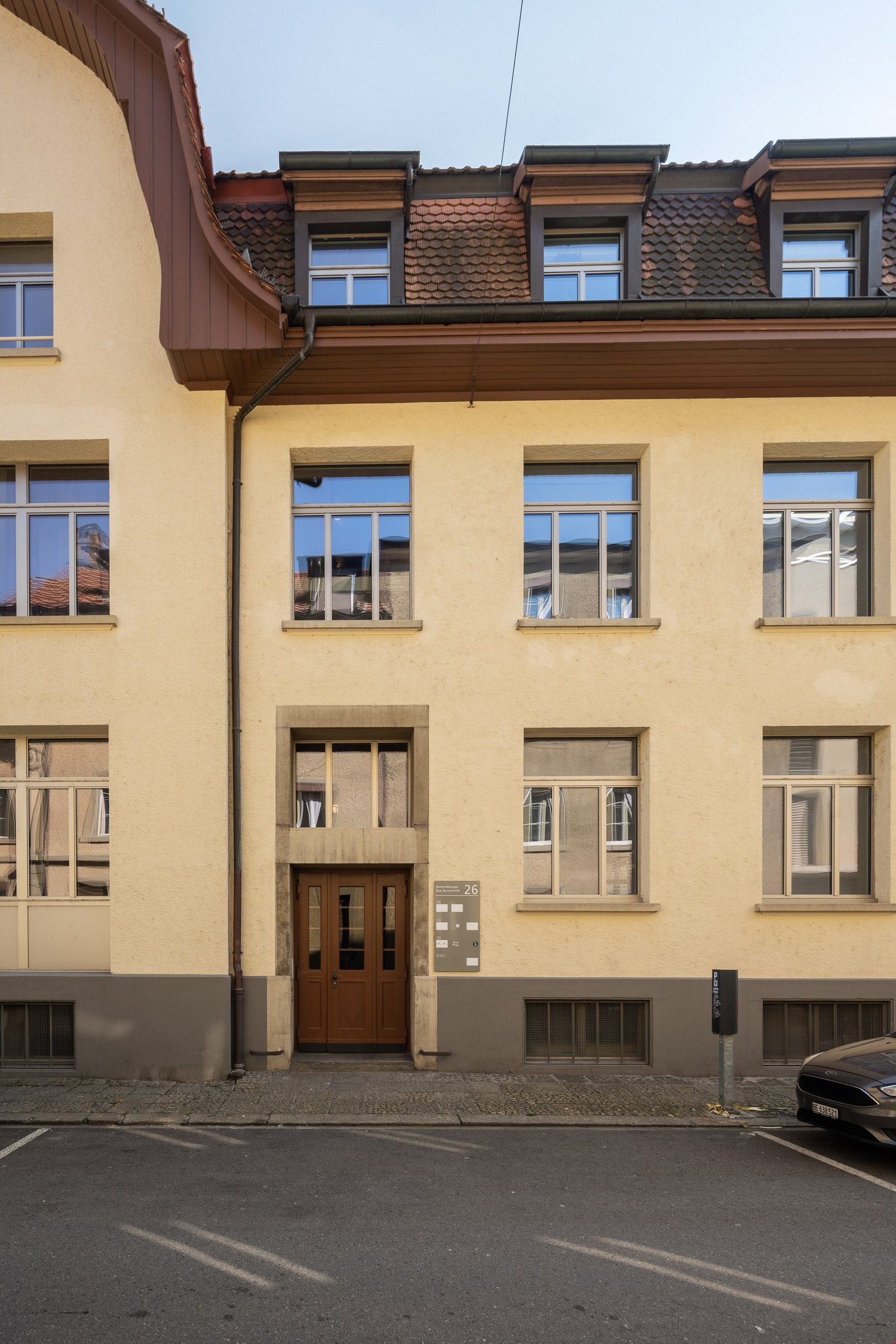 Four story building, double doors, many windows, parking space, gray color, brick facade