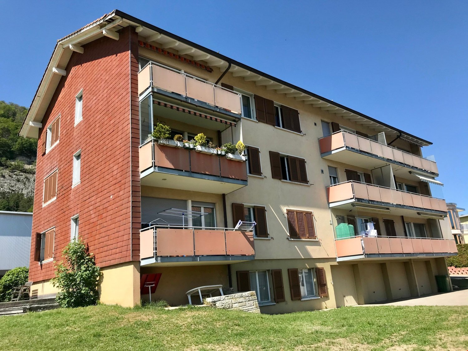 4 story apartment building, red brick, beige wall, multiple balconies, green plants, grassy lawn