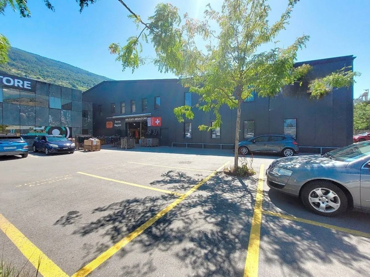 large parking area, black building with glass windows, tree, clear blue sky