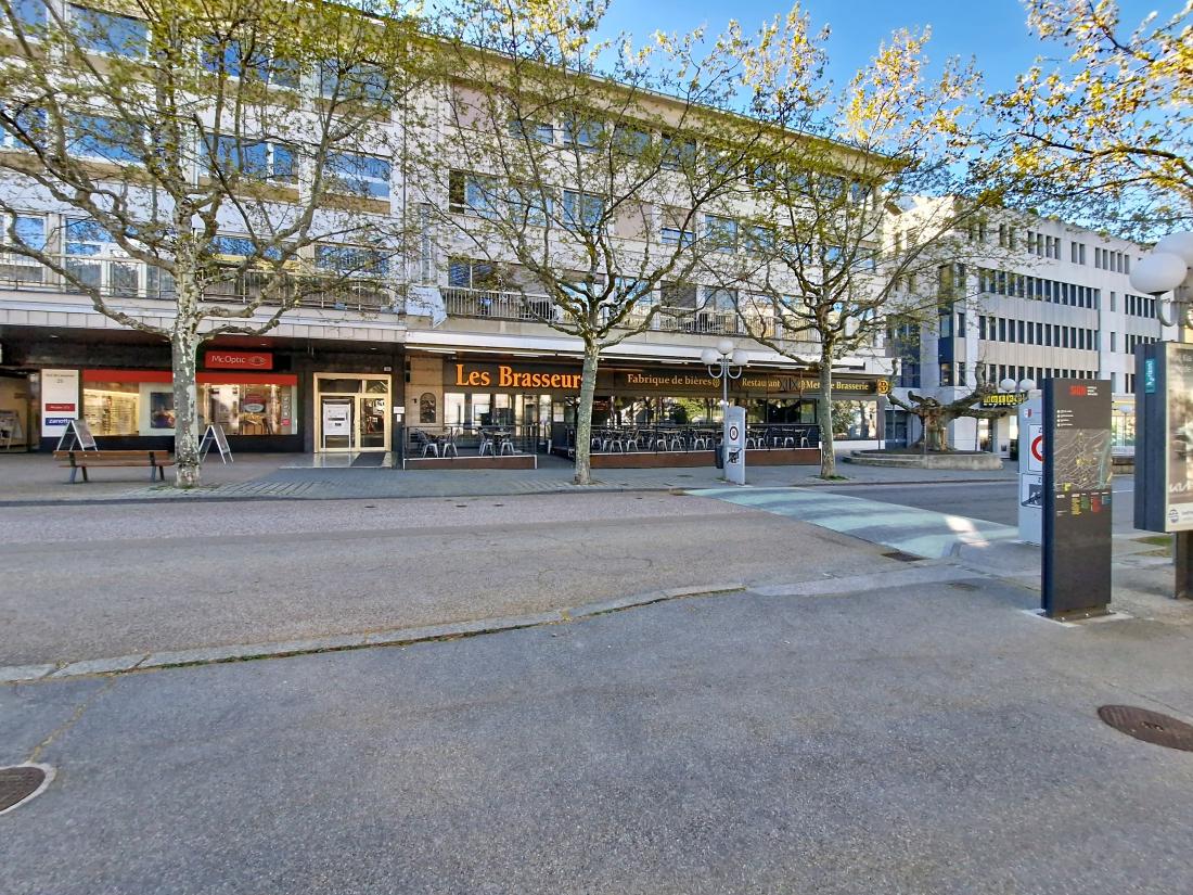 A building with many windows, a restaurant named Les Brasseur, a bench, and trees in front.