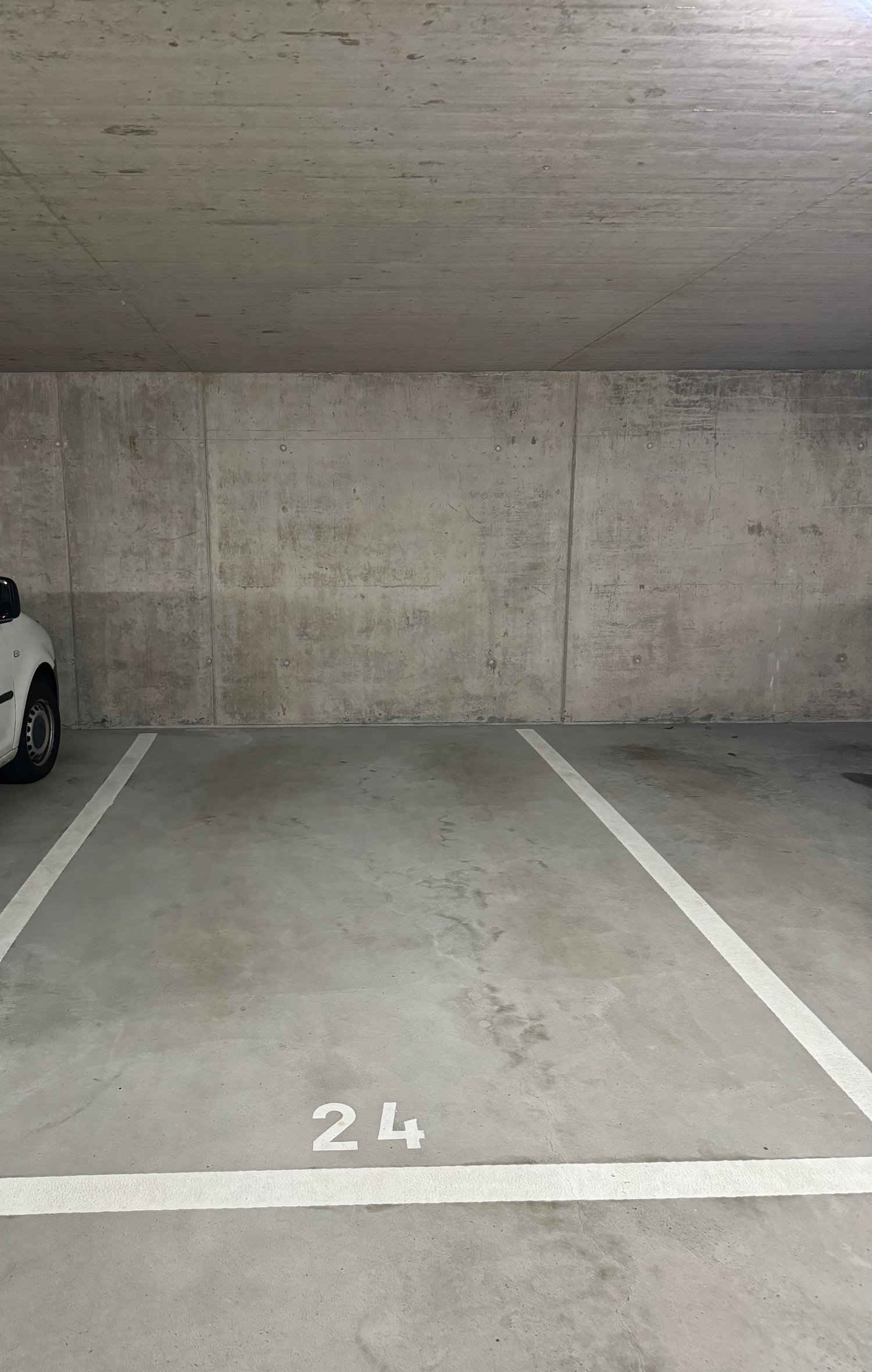 A concrete parking area with two white-marked parking spaces, marked with number '24' and empty