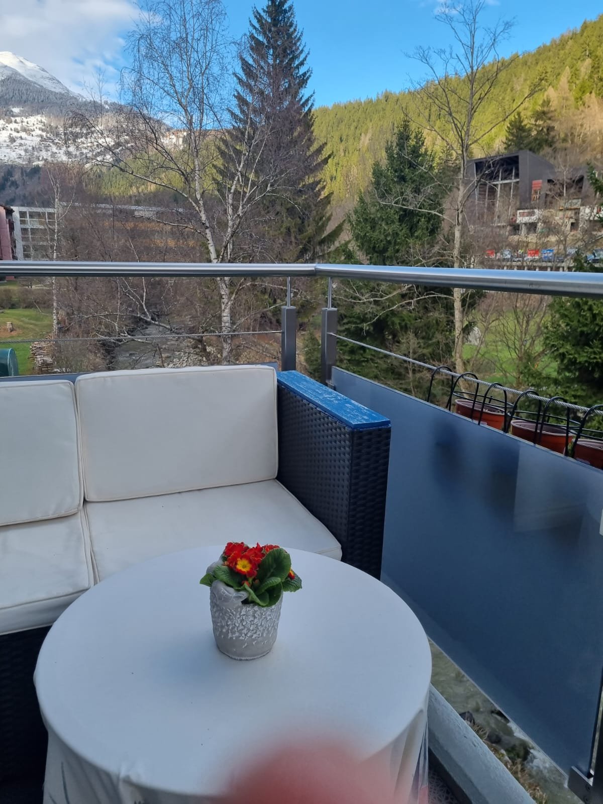 white couch, flower on table, fenced balcony, mountain view