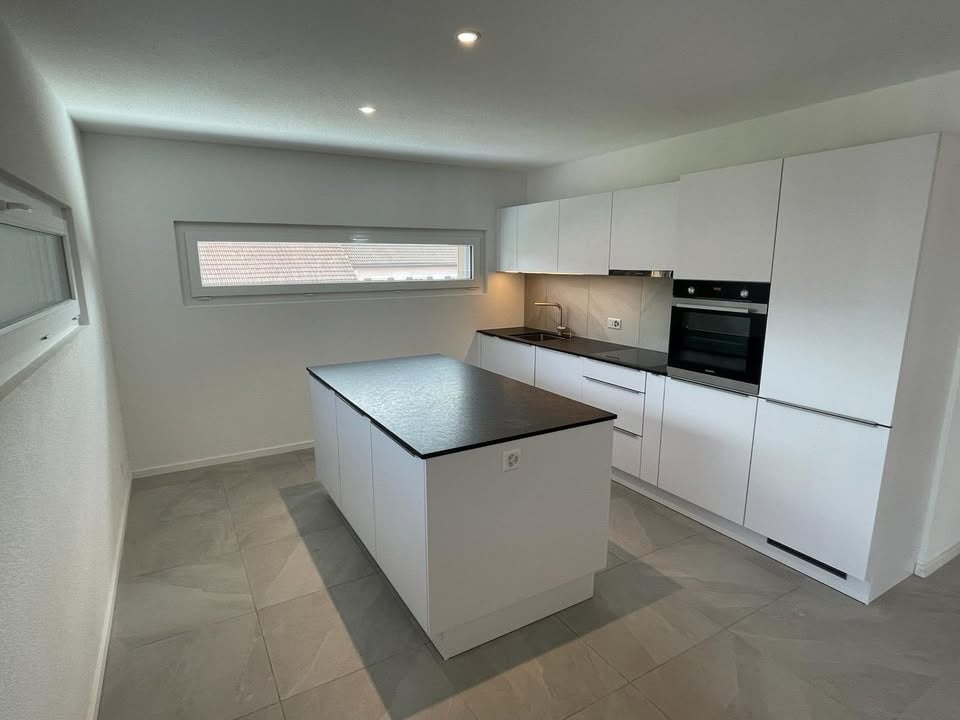 Modern kitchen with island, white cabinets, black countertops, built-in oven and microwave, sink with faucet, and tiled flooring.