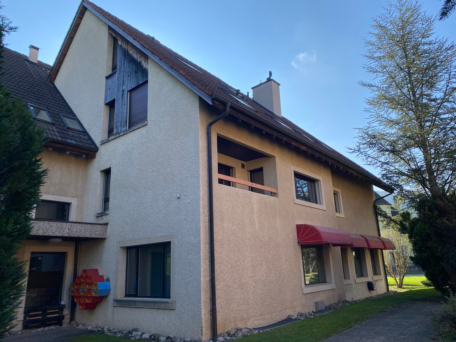 2 story house, beige exterior, brown roof, red awnings, balcony, windows, chimney