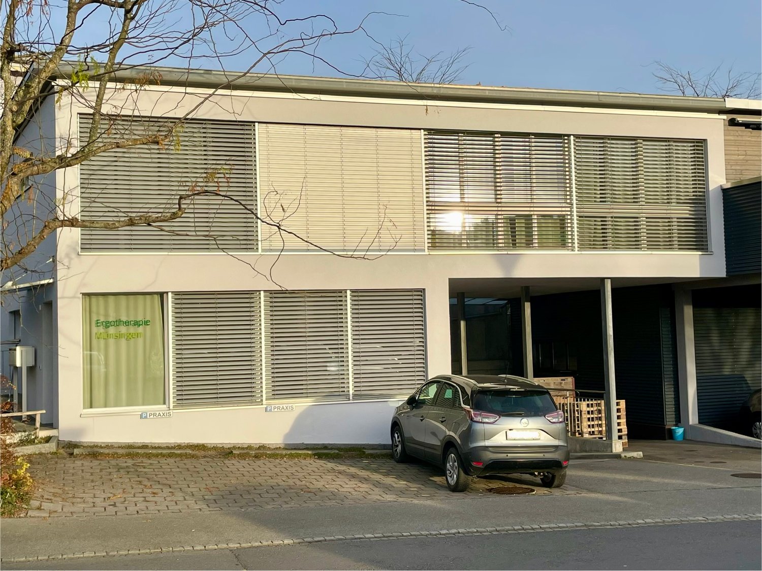 modern white building with many windows, a car parked in front, grey brick paving in front