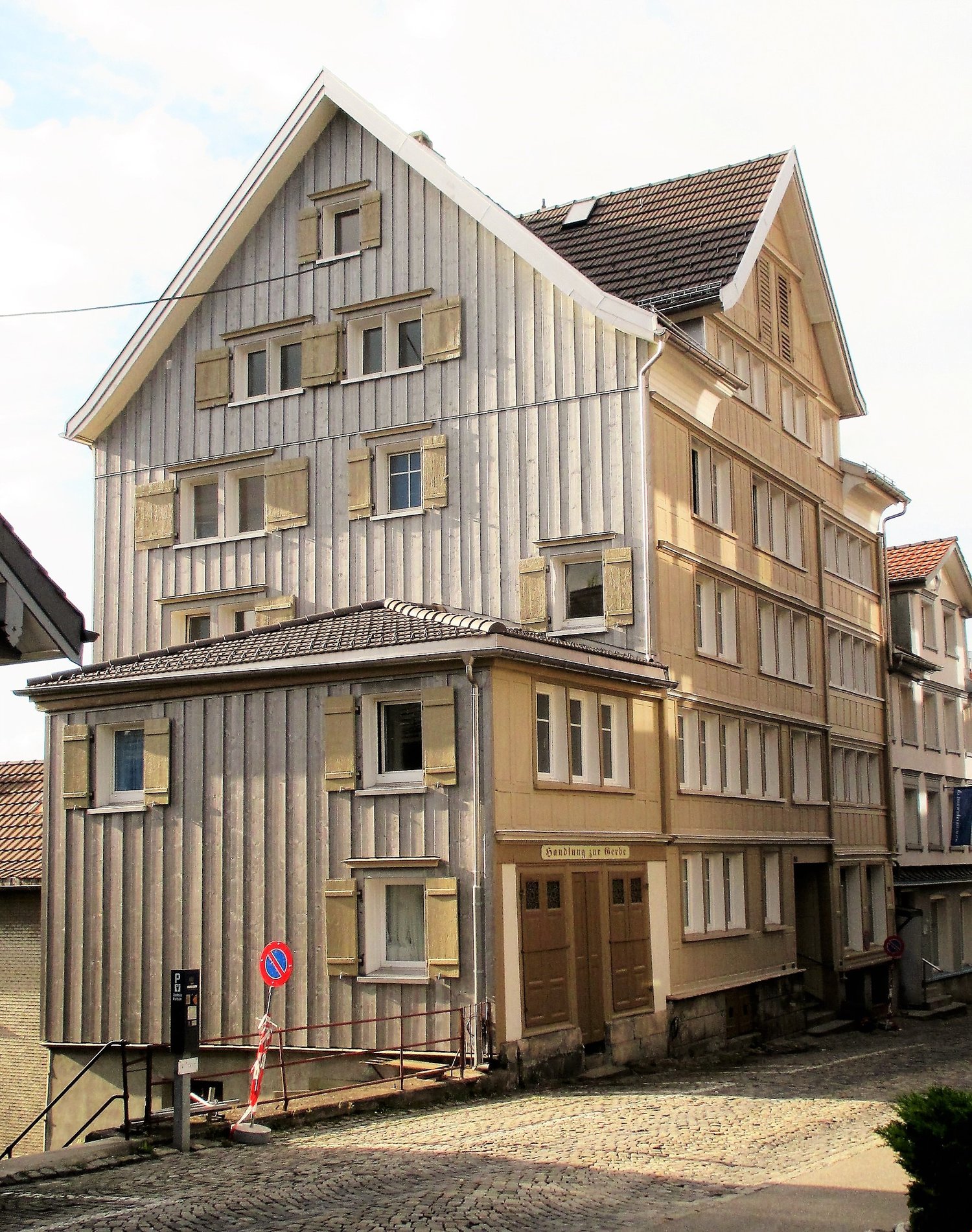 3 story building, wooden exterior, multiple windows, brown doors, cobblestone street