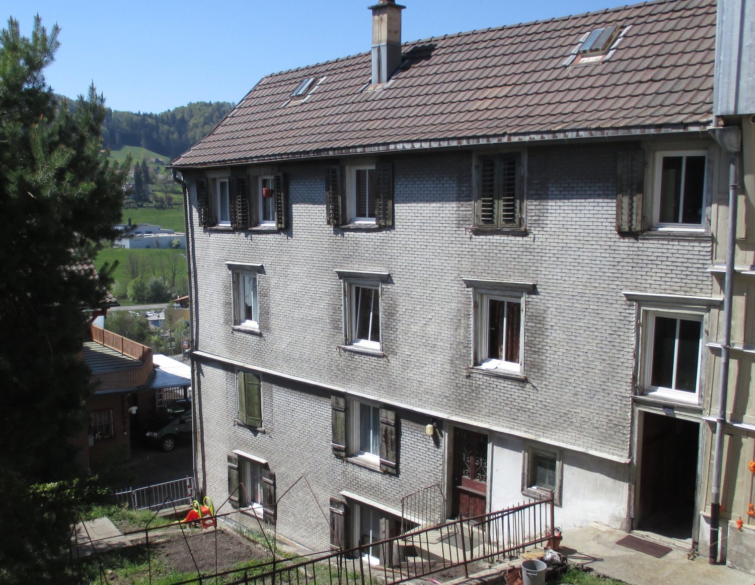 3 story house, brick exterior, 4 windows on each floor, brown roof, chimney, fenced pathway