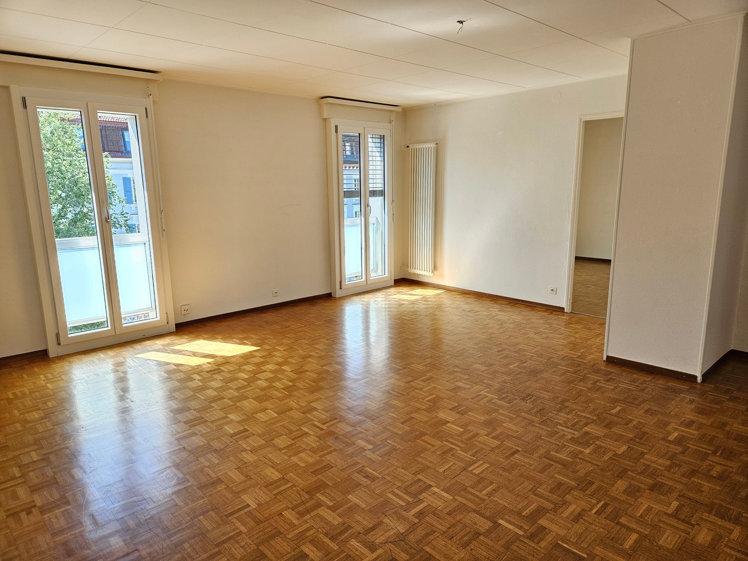 Empty room with double doors, large windows, wooden parquet floor, white walls