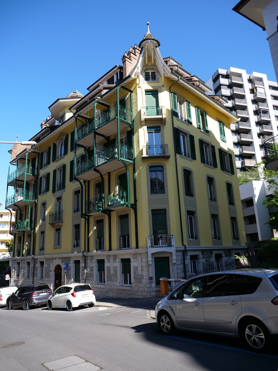 large yellow building with green accents, 4 balconies, multiple cars parked in front