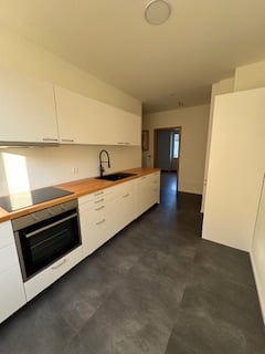 modern kitchen with white cabinets, wooden countertops, black floor, integrated oven, dishwasher, washing machine
