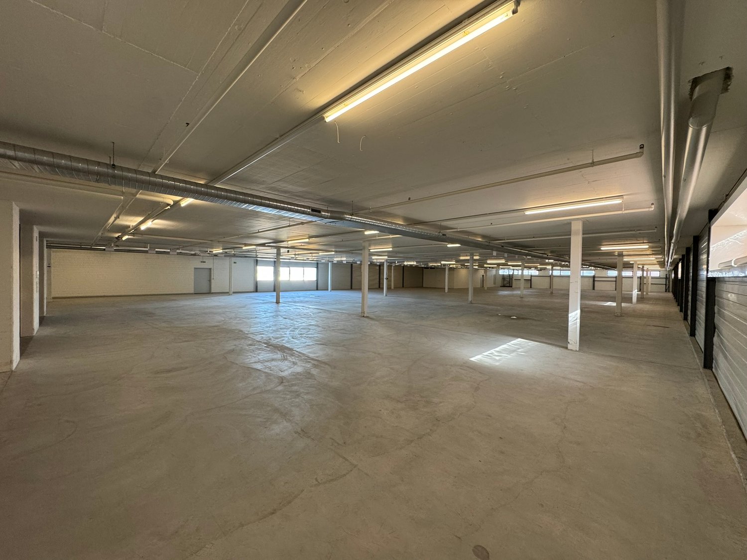 empty large space, industrial setting, white walls, exposed beams, windows, pipes