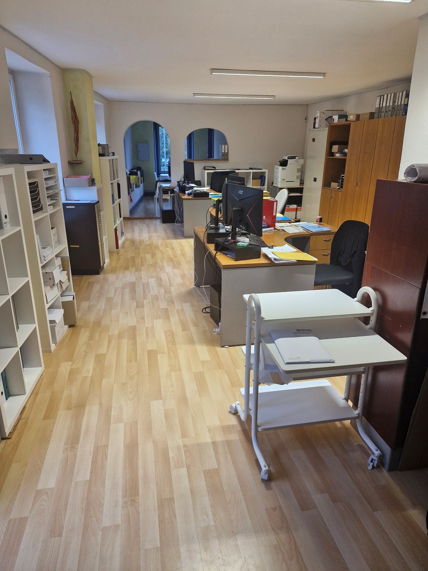 Modern office with desks, computers, bookshelves, and storage units, parquet flooring, office equipment
