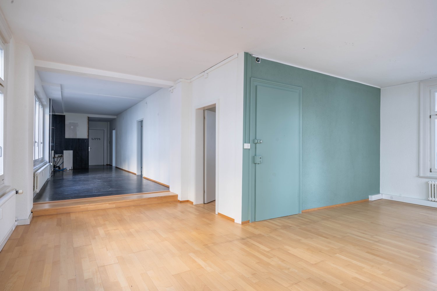 empty room with wooden floors, white and green walls, radiators, and multiple windows