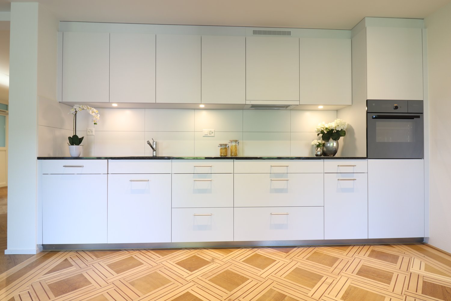 modern, white cabinets, black countertop, stainless steel sink, oven, flowers on countertop, wooden floor