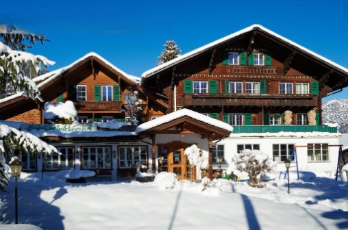 2 story brown wooden house, green windows, snow covered, balcony on the first floor