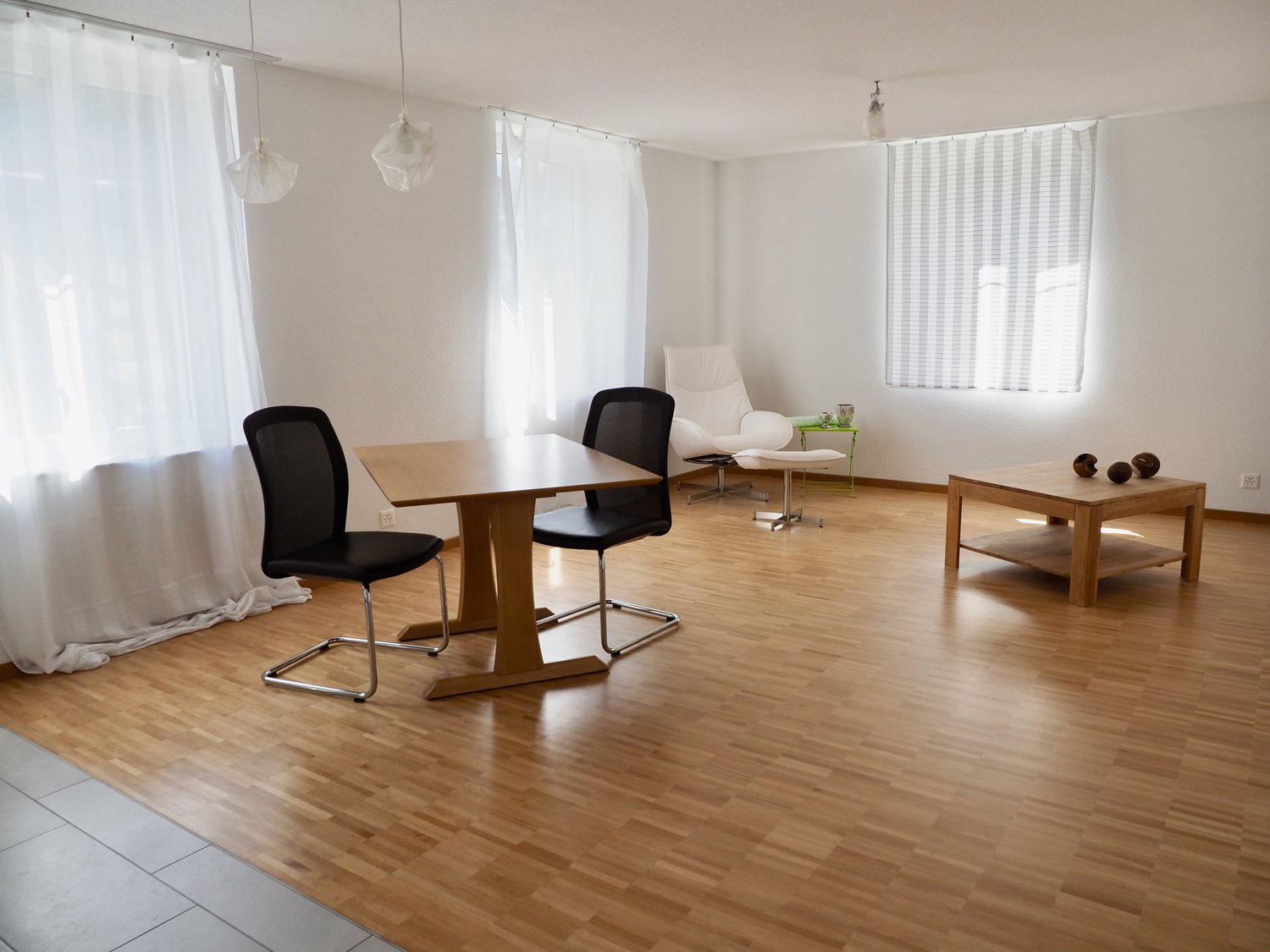empty room, wooden floor, white walls, curtains, wooden table, two chairs, white armchair, green table, table lamp