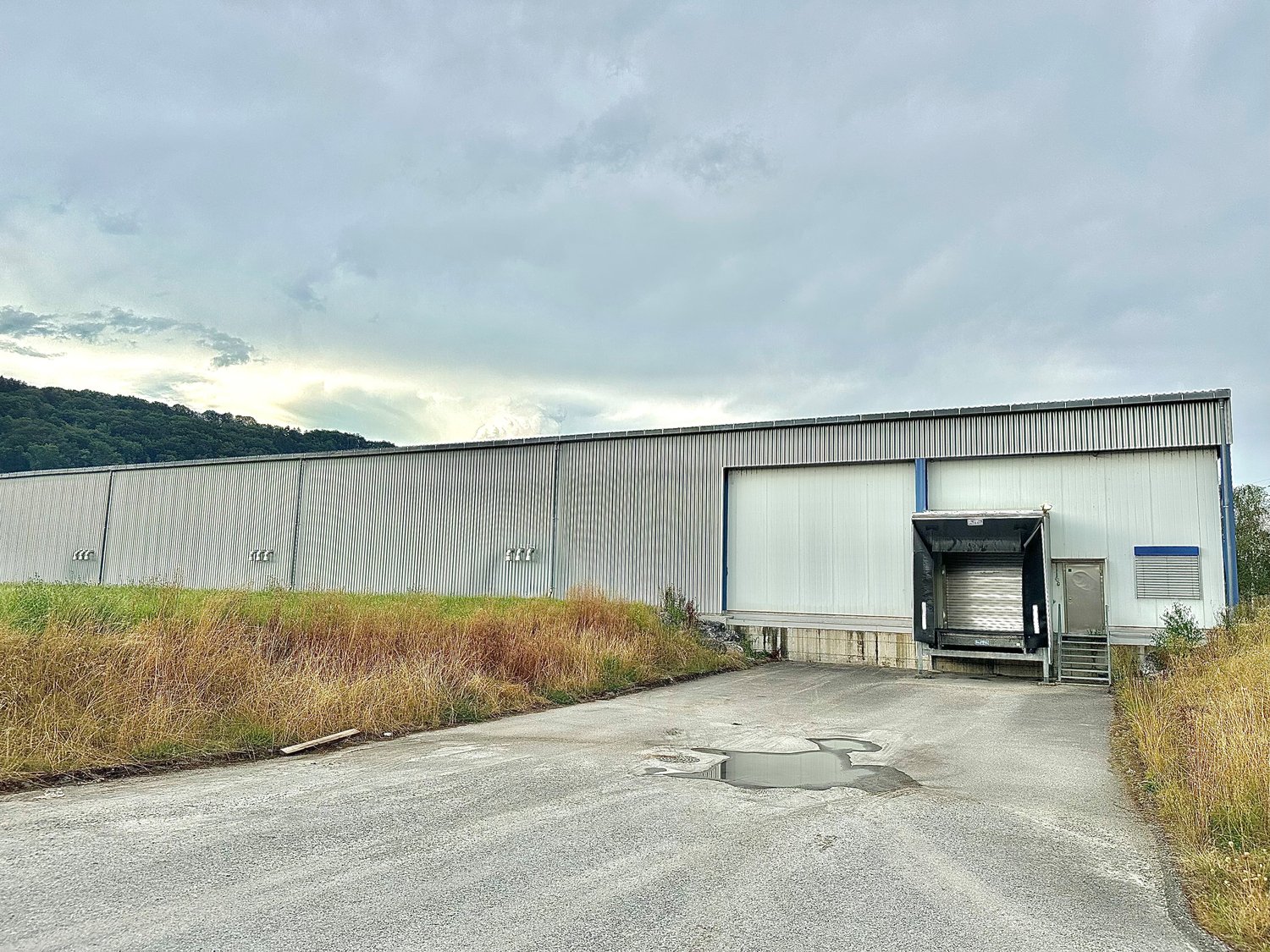 Large industrial building with one main entrance, a large opening on the side, and a smaller building next to it. Parking lot in front.