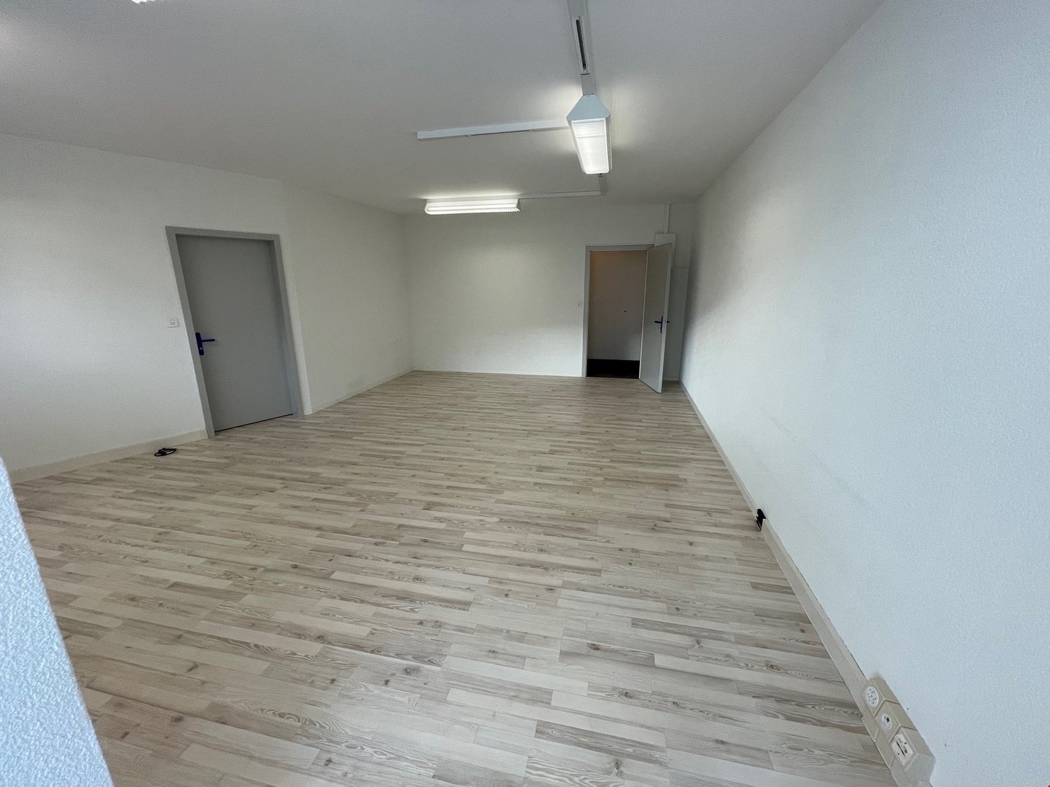 empty room with wooden floor, two doors, and fluorescent ceiling lights