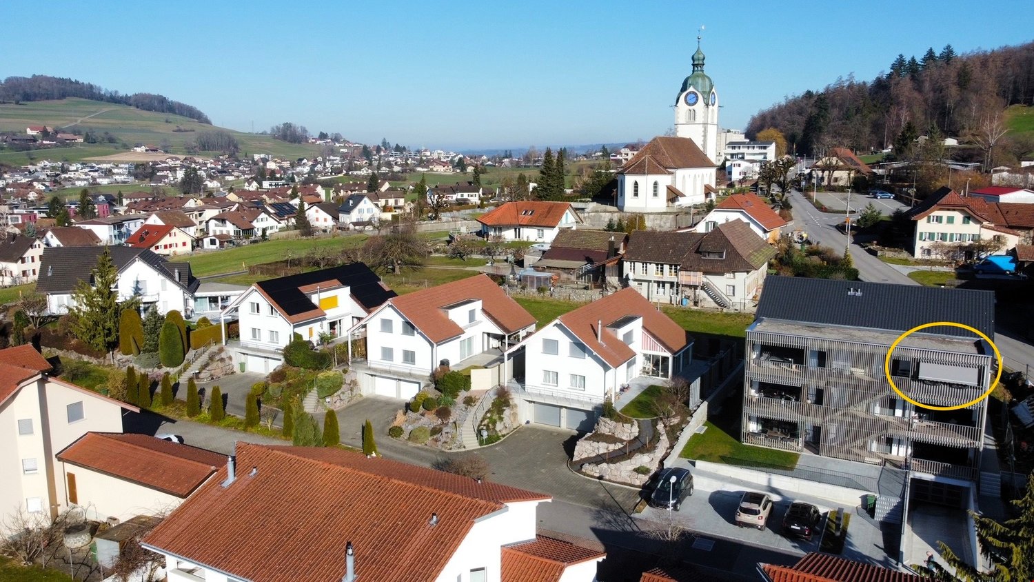 Aerial view of a neighborhood with several houses, one of which has a yellow circle highlighting a balcony