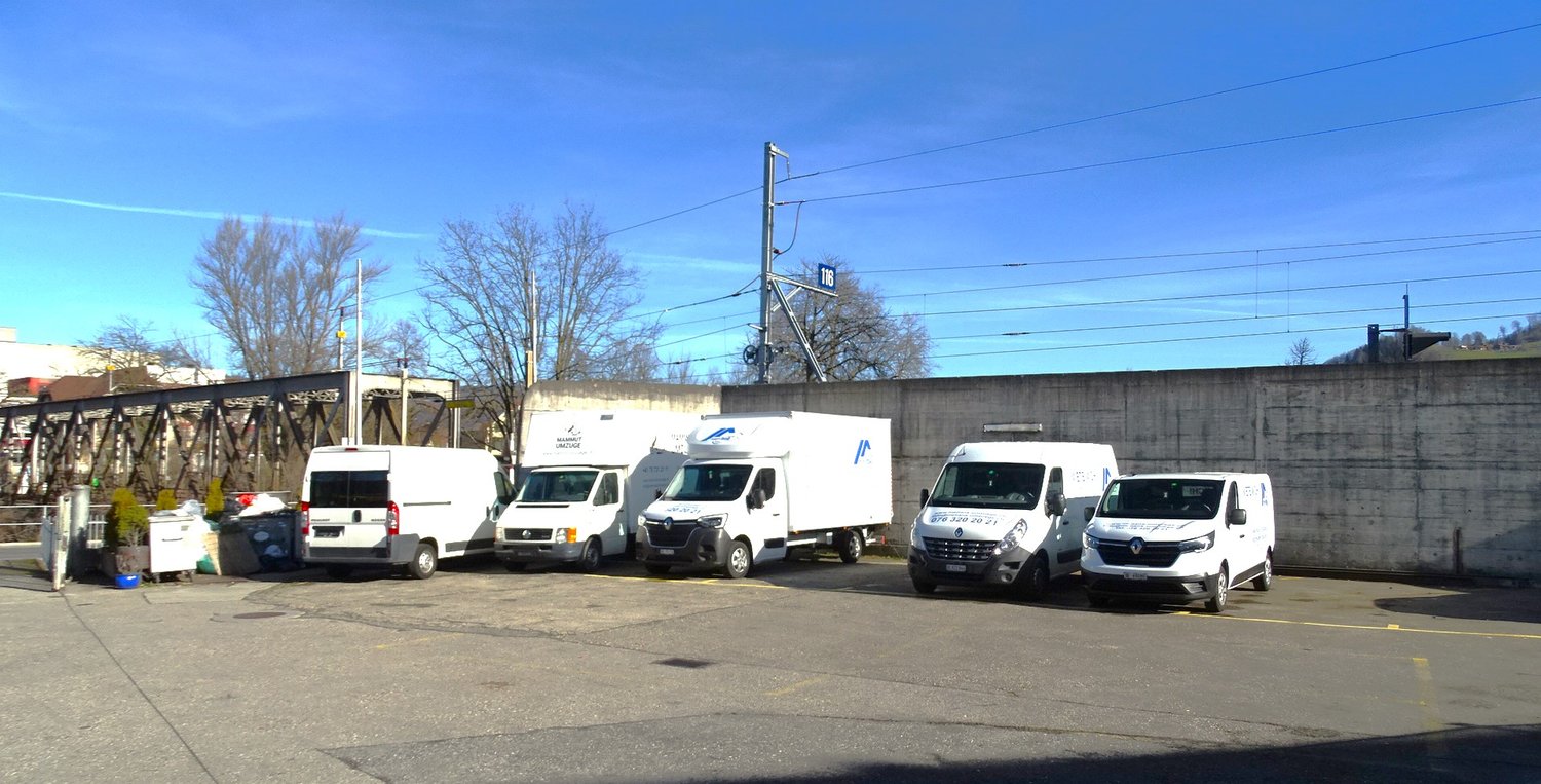 Several white vans parked in a lot with an electric pole and power cables.