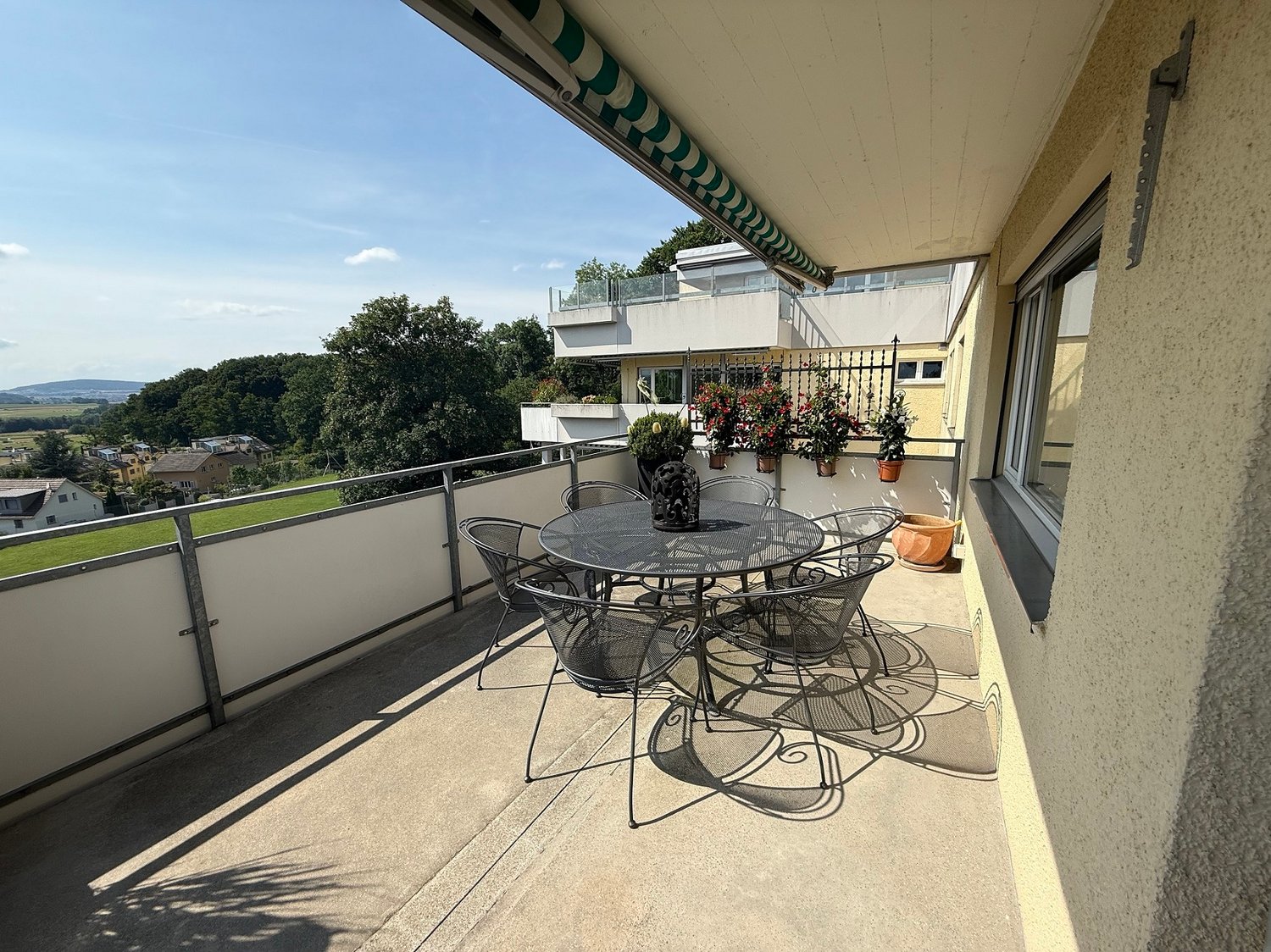 outdoor dining table with chairs, railing, plants, view of greenery