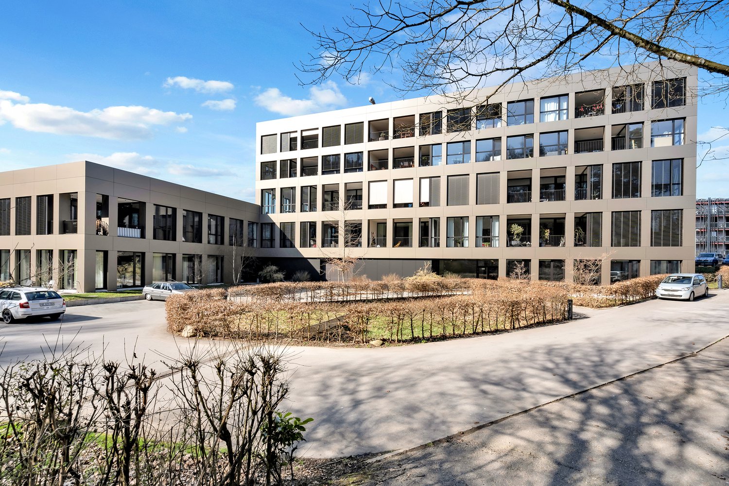 3 story apartment building, grey panels, glass windows, car parking in front