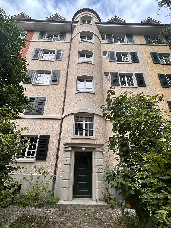 5 story building, cream color, black shutters, brick base, centered door, tree in front